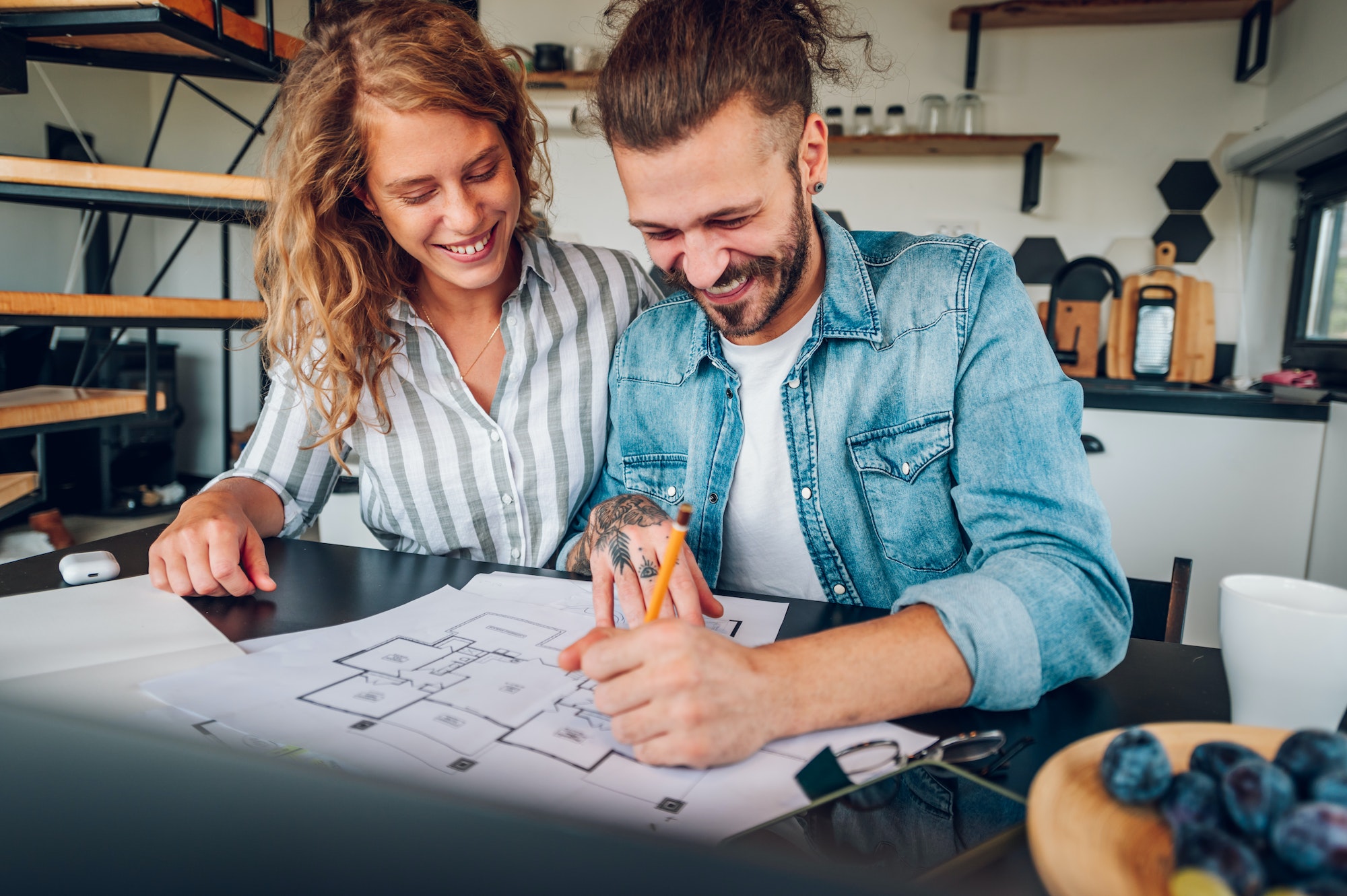 Happy couple using laptop and looking into blueprints of their new home